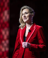 A headshot of Ms. Tara Murphy Dougherty speaking in a red blazer infront of a red curtain